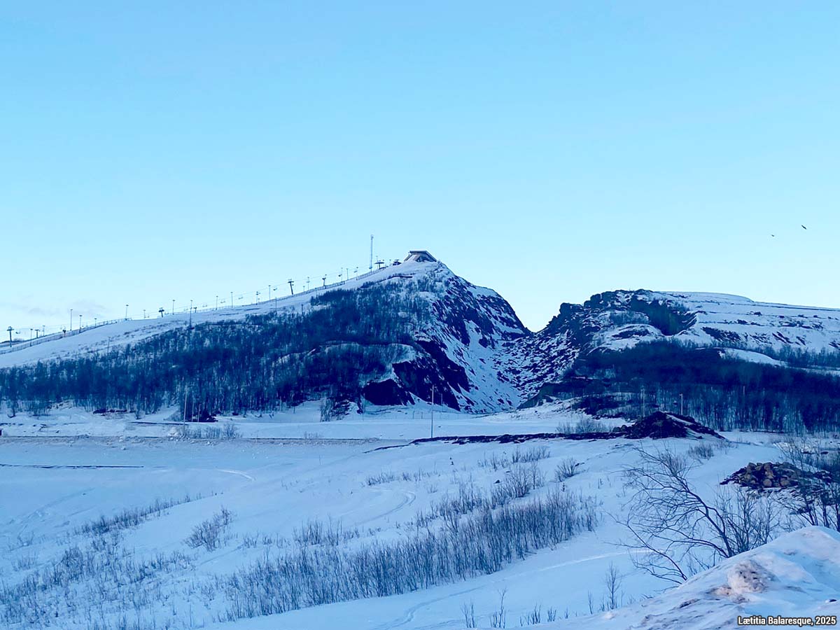 La montagne Luossavaara, où se trouvait la première mine à ciel ouvert, a été aménagée en piste de ski. On aperçoit un effondrement de terrain au milieu. L’exploitation pourrait recommencer puisqu’un gisement de phosphore y a été récemment découvert. Cliché de Lætitia Balaresque, février 2025. La montagne Luossavaara